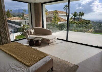 Dormitorio con grandes cristaleras y vistas al mar. Decorado con tonos neutros.